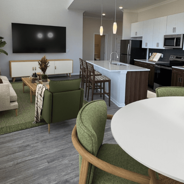 Alto Apartments Open Floor Plan Concept A modern living room with a loft design features a metal staircase leading to an upper level. Two large windows with blinds allow natural light to fill the space. The room includes a gray couch, a coffee table with a glass fireplace, and a floor lamp.